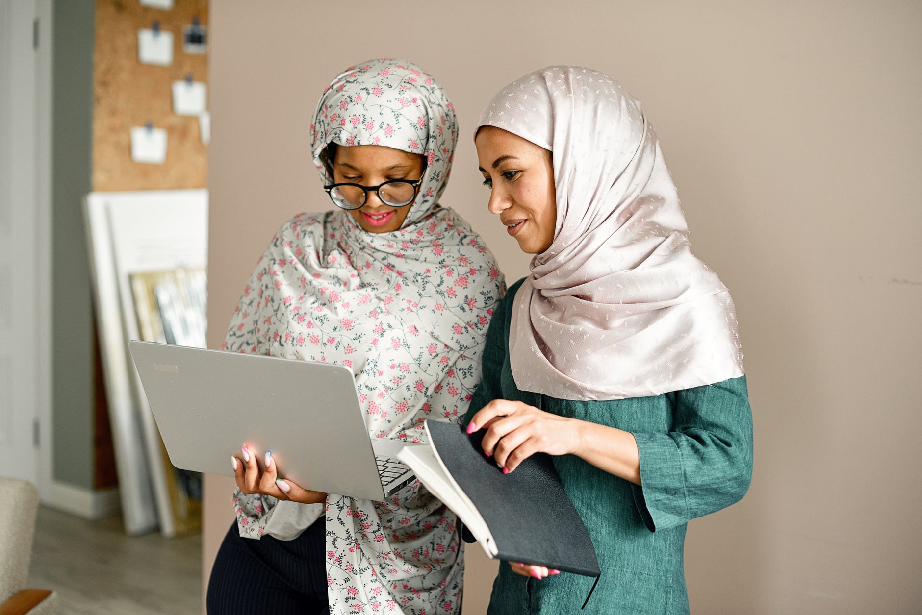 women in hijab standing and using a laptop